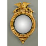 A Regency giltwood convex mirror, circular, with ebonised slip and eagle pediment.