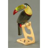 A Swarovski crystal toucan, Roland Schuster, grey, yellow, red and chrome, with wooden stand.