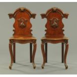 A pair of Victorian oak hall chairs, with armorial shields, solid seats and raised on cabriole legs.