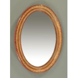 An early 20th century simulated red tortoiseshell oval framed mirror with gilt highlights.