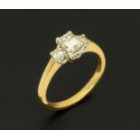 An 18 ct gold two tone ring, set with an emerald cut diamond and diamond to each shoulder,