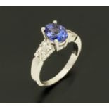 An 18 ct white gold ring, set with an oval tanzanite and diamonds to each shoulder, size M/N.