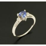 An 18 ct white gold ring, set with a triangular tanzanite and diamond to each shoulder, size L/M.