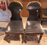 A pair of ebonised hall chairs with shaped backs and gilted top rails with turned legs