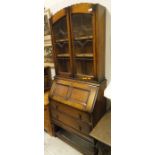 An oak bureau/bookcase with leaded glazed doors enclosing shelves above the fall and two drawers,