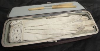 A velvet covered glove box containing various ladies white leather gloves and a pair of bone glove