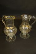 A pair of 19th Century cut glass and gilt decorated jugs with swag and bow motifs,