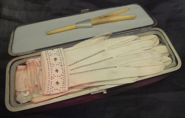 A velvet covered glove box containing various ladies white leather gloves and a pair of bone glove