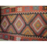 A Kilim rug, the central panel set with repeating lozenge shaped medallions in green, black, pink,