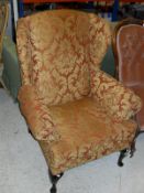 A pair of terracotta and gold brocade upholstered wing back scroll arm chairs on cabriole legs to