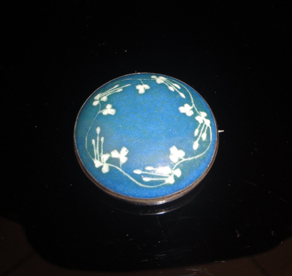 A Ruskin ceramic brooch decorated with floral motifs on a blue ground, stamped "Ruskin" to back,