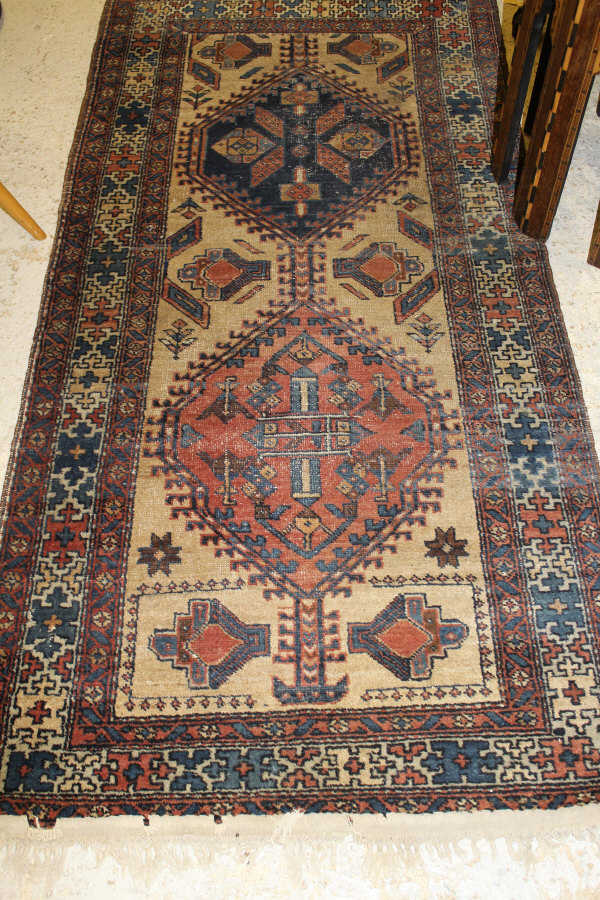 A Caucasian rug, the central panel set with two joined lozenge shaped medallions on a fawn ground,