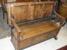 An early 20th Century oak monk's bench with folding top above a panelled front with blind fretwork