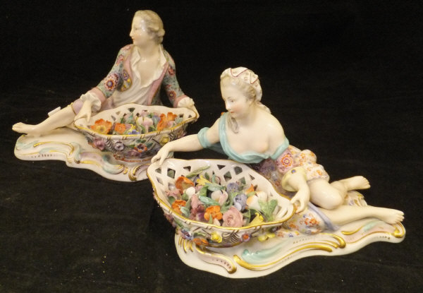 A pair of 19th Century Meissen figures as a recumbent gentleman and lady with baskets of flowers,