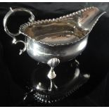 A George III silver sauce boat with C scroll handle and raised on hoof feet with embossed bead