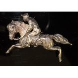 A white metal brooch in the form of a horse and jockey in half striped silks, bears Registration No.