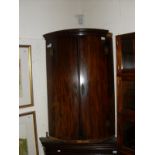 An early 19th Century mahogany bow fronted hanging corner cupboard with three shelves
