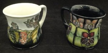 A Moorcroft Violet pattern mug, together with a Moorcroft Blackberry pattern mug,