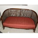 An early 20th Century mahogany framed bergere sofa with upholstered seat on hairy paw feet,