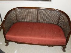 An early 20th Century mahogany framed bergere sofa with upholstered seat on hairy paw feet,