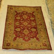 A modern Persian style rug, the central panel set with repeating floral design, on a red ground,