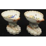 A pair of early 19th Century Berlin porcelain salts as bird and insect decorated shells held aloft