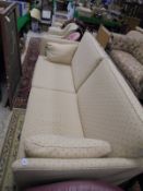 A three seat sofa upholstered in fabric with a cream ground and repeating terracotta pattern