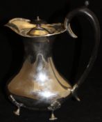 A George V silver water jug of baluster form raised on four acanthus moulded feet with ebonised