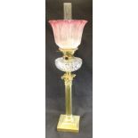 A brass and glass table oil lamp with cranberry rimmed and flower etched glass shade above a cut