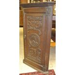An early 19th Century oak wall hanging corner cupboard with a single heavily carved door with the