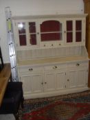 A cream painted dresser with two glazed doors enclosing shelves with central open shelves and three