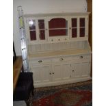 A cream painted dresser with two glazed doors enclosing shelves with central open shelves and three