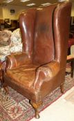 A 19th Century high backed wing back arm chair in brown leather raised upon mahogany cabriole legs