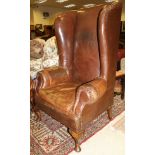 A 19th Century high backed wing back arm chair in brown leather raised upon mahogany cabriole legs