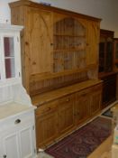 A large pine dresser with ogee moulded pediment above various open recesses flanked by cupboard