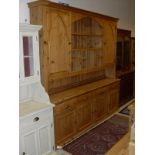 A large pine dresser with ogee moulded pediment above various open recesses flanked by cupboard