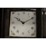 An oak cased long case clock with Roman numerals to the enamel dial and floral sprays to the