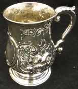 A Victorian silver mug with embossed fruit and scrolling decoration raised on a circular foot (