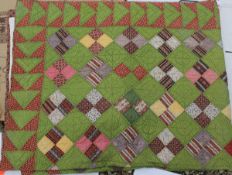 A 19th Century quilt of square design with green ground and multi-coloured patches on a patterned
