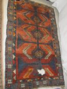 A red ground Kazak rug, the central field with three hooked medallions in blues, yellows,