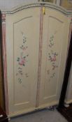 A cream painted two door wardrobe with floral and fruit design raised upon bun feet,