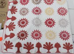 A 19th Century quilt with red stylised sunburst and floral motifs on a white ground with plain
