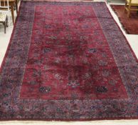 A Persian rug, the central panel with repeating floral sprays on a puce ground,