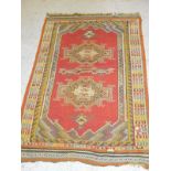 An Eastern red ground rug with two lozenge shaped medallions to the central field in yelllow,