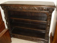 A late Victorian carved oak Gothic revival open bookcase with cushion drawer over two adjustable