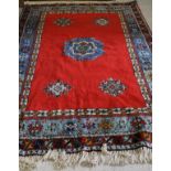 A 20th Century Turkish rug, the central panel set with geometric medallions on a bright red ground,