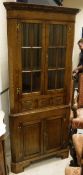 An oak corner display cupboard with dentil cornice above two astragal glazed doors enclosing