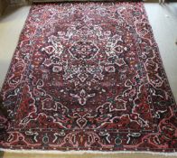 A Persian burgundy ground carpet with central stepped floral medallion in shades of salmon, black,