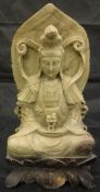 A Chinese carved grey soapstone figure of Guan Yin serated cross-legged holding book and vase upon