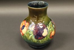 A William Moorcroft baluster shaped vase with floral decoration on a blue green ground,